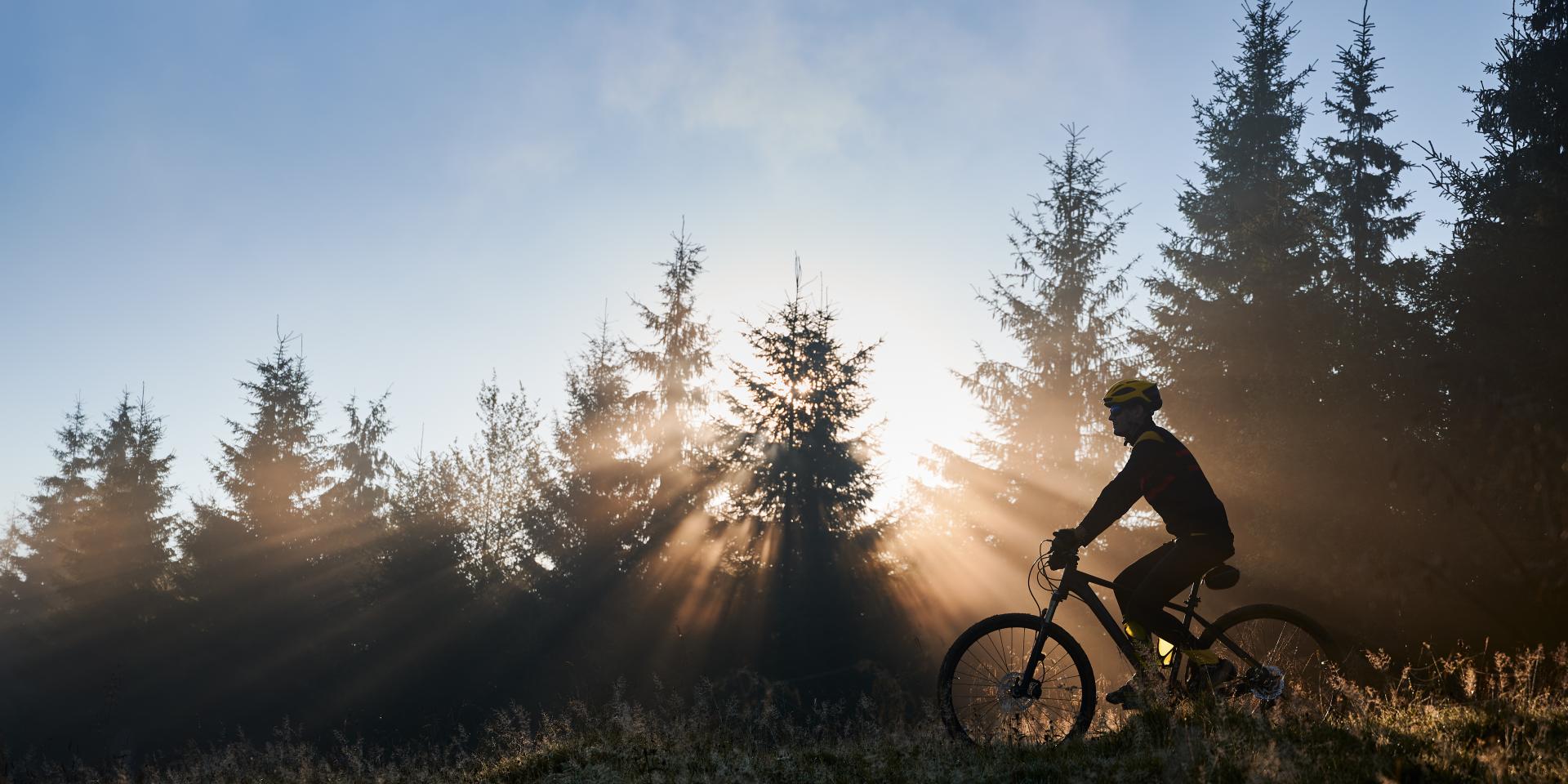 Jeune homme pratiquant le VTT en milieu naturel, avec le lever du soleil en fond